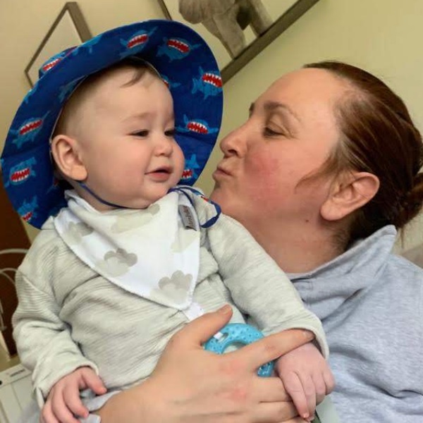 Baby Alex in a shark sun hat while his mother kisses his cheek.