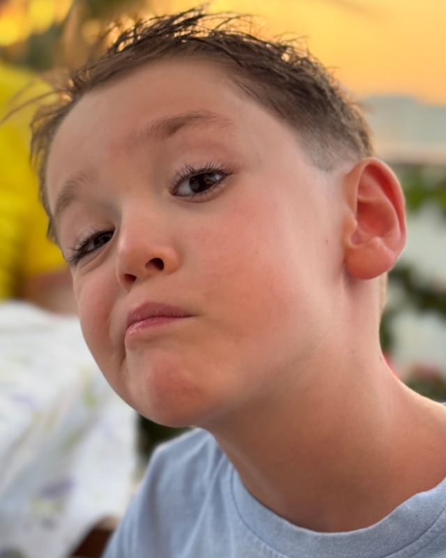 Alex at a summer dinner table, chin tucked and eyebrow raised in a mock-serious face.